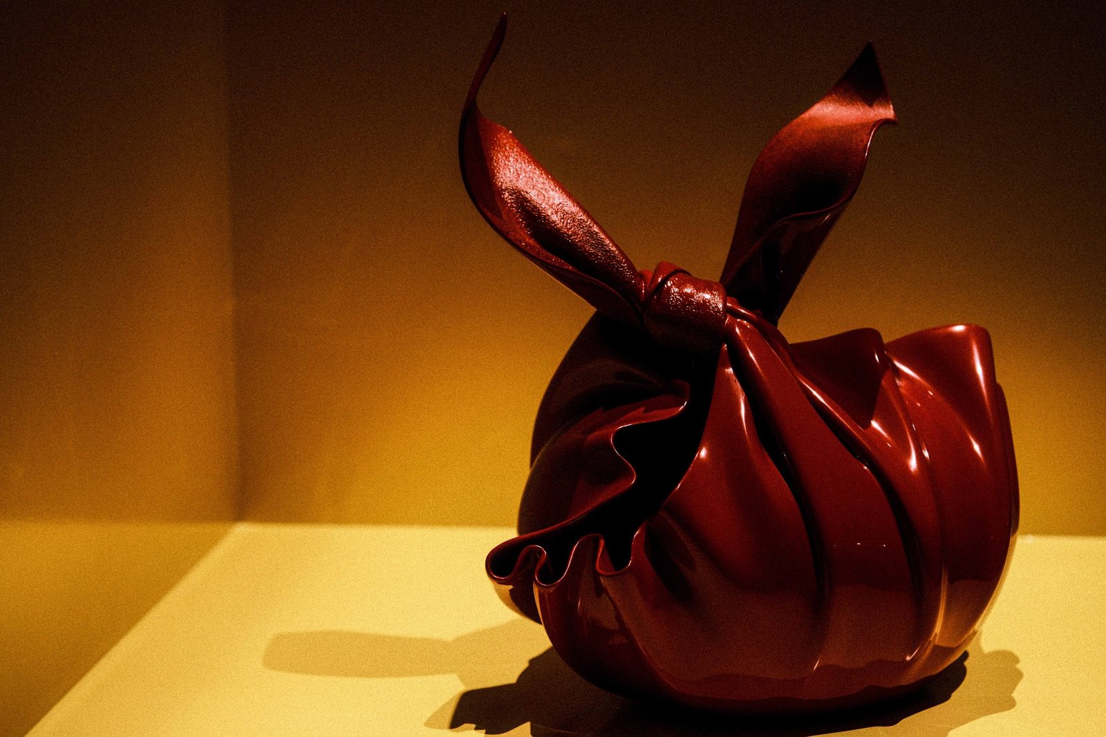 A sculptural glass form in deep red with flowing, ribbon-like shapes