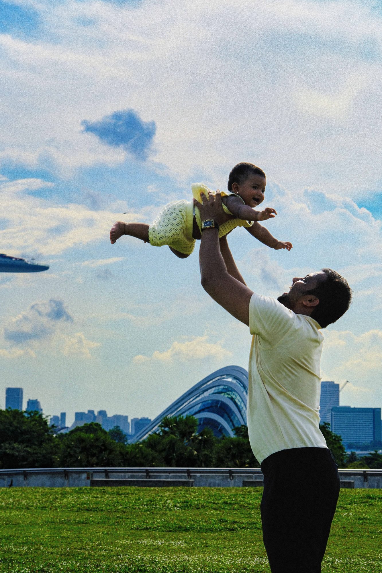 Father joyfully lifting his toddler up against a city skyline