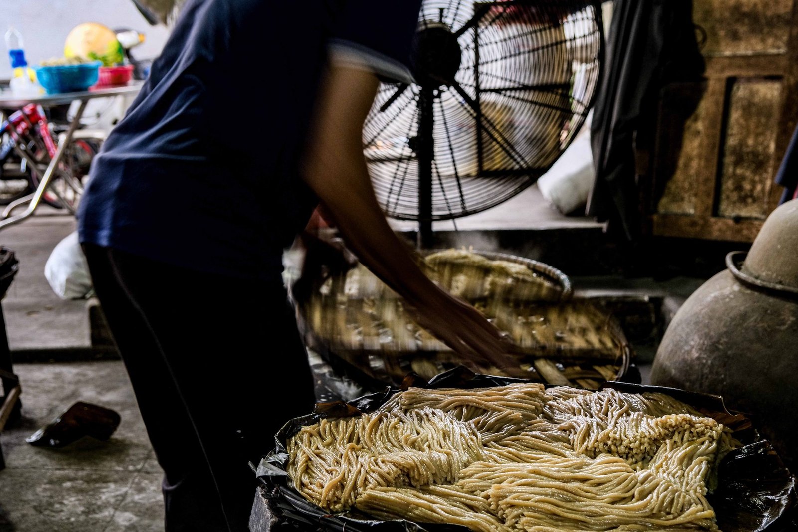 Worker flattening dough by hand over a large steel pan in Vietnam